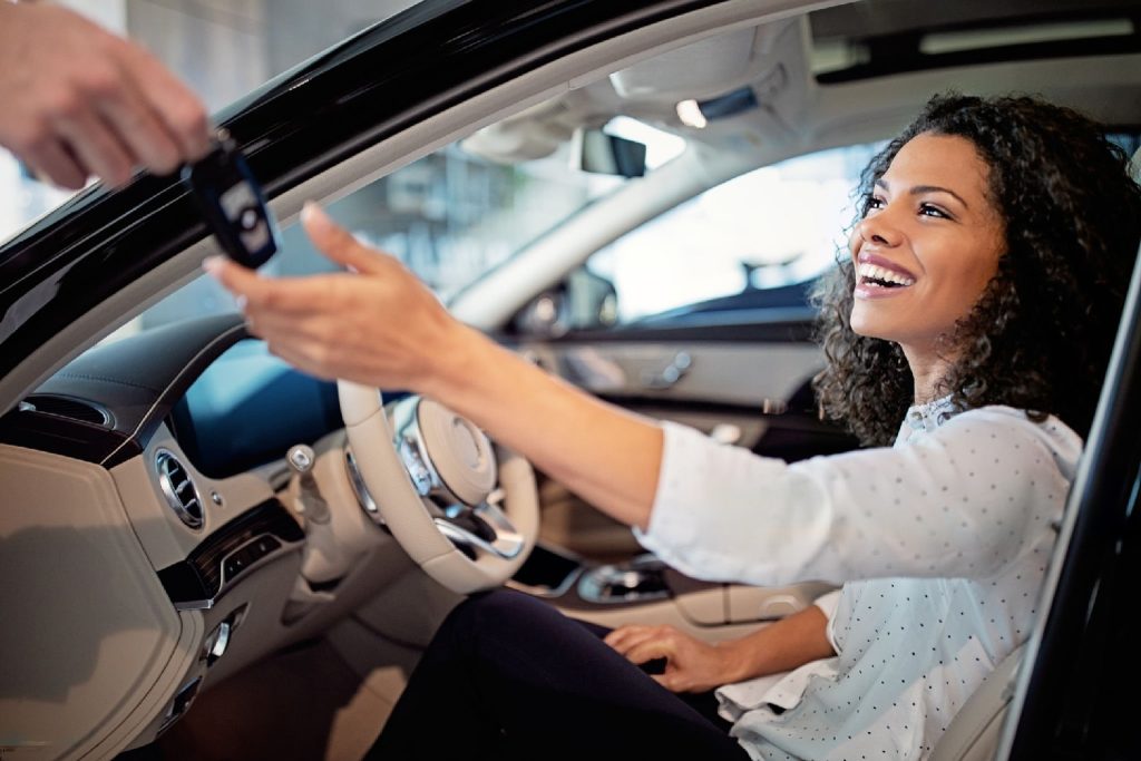 a female happily taking the keys of a new car while sitting inside