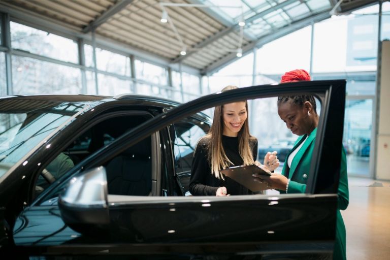 old lady signing a contract while standing beside a car
